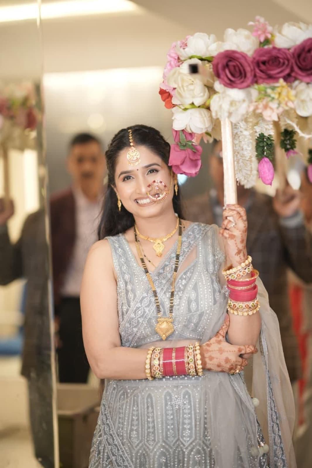 Bridal entry portrait with glowing skin and soft eyes on a smiling bride in a silver lehenga holding a floral phoolon ki chadar