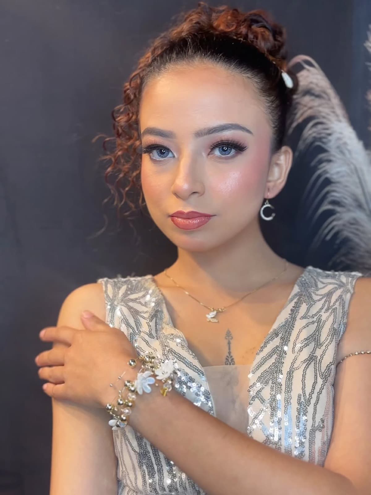 Party glam makeup with defined eyes, highlighted skin, and neutral lips on a client in a silver sequin gown