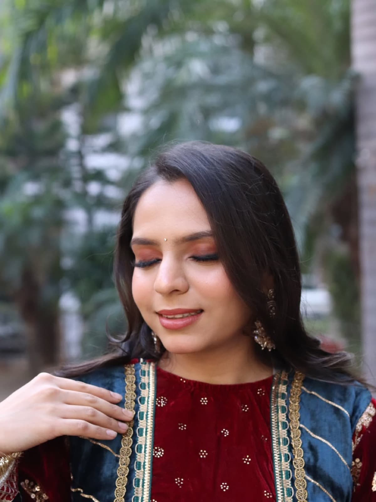 Close-up of warm rose-gold eye makeup with soft lashes and peachy skin on a client in a maroon velvet suit