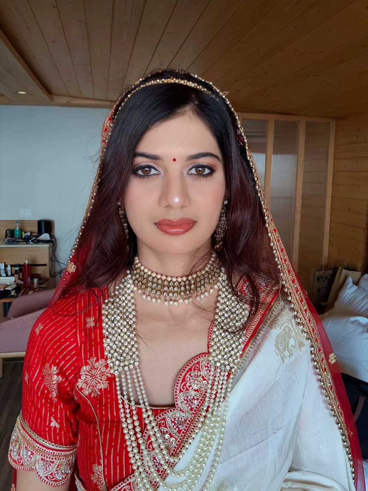 Bridal makeup close-up with terracotta lips, defined brows, and pearl-and-gold kundan jewellery on a bride in a red and white saree
