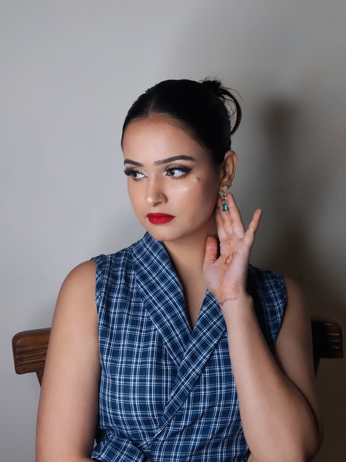 Editorial-style makeup with bold red lips, sharp winged liner, and sleek bun on a client in a blue plaid blazer dress