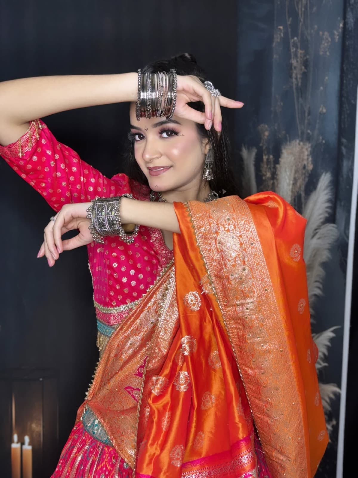 Dynamic garba night look with pink blush, braided updo, stacked oxidized bangles, and pink banarasi lehenga with orange dupatta