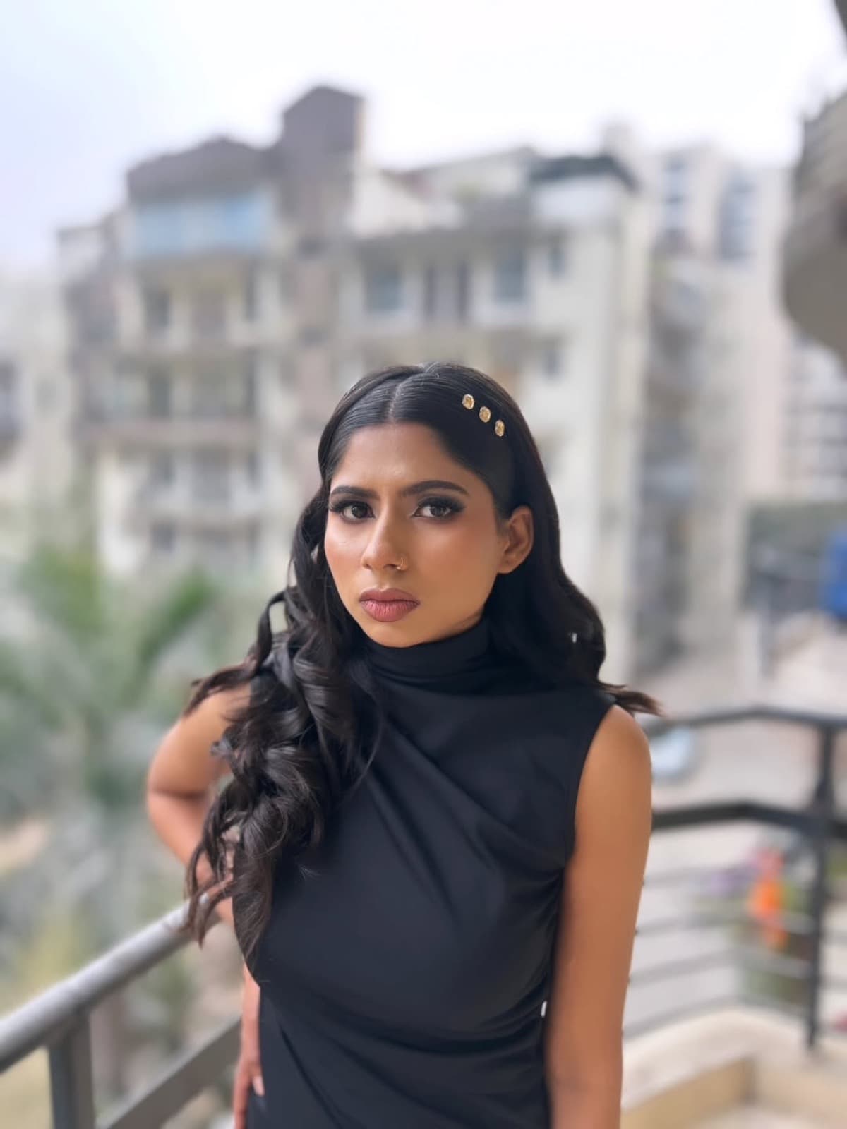 Sleek party glam with smokey eyes, nude lips, gold hair clips, and curled waves on a model in a black turtleneck, balcony setting