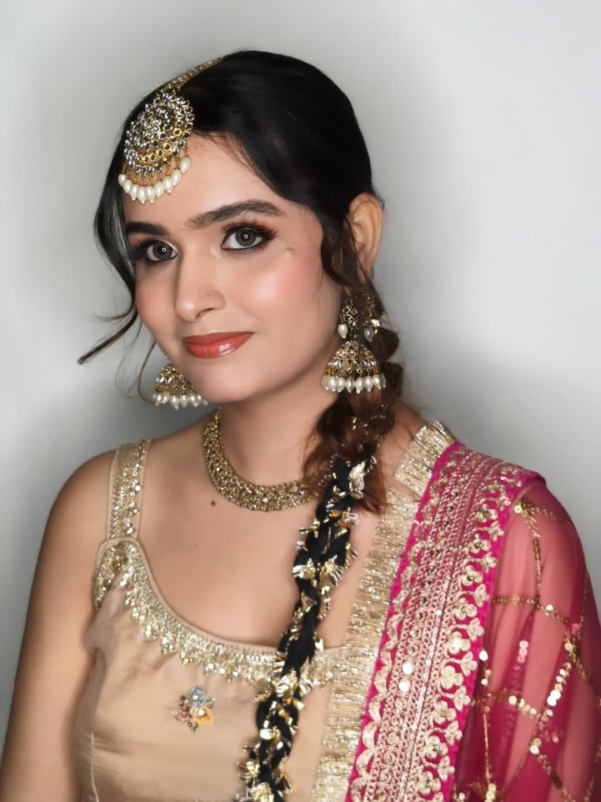 Bridal makeup portrait with glowing skin, soft smokey eyes, and maang tikka on a bride in a champagne lehenga with pink dupatta